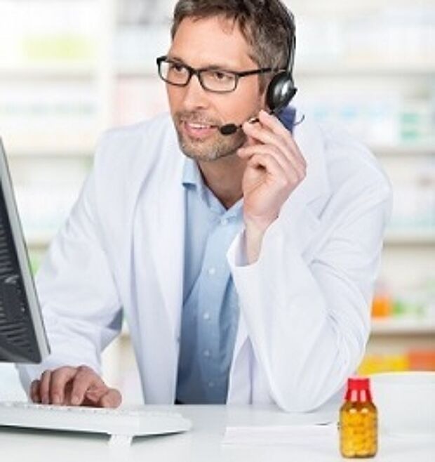 Person im weißen Kittel tippt auf einer Computer Tastatur und im Vordergrund steht ein Medikament
