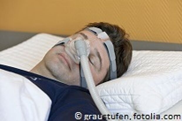 Mann liegt im Bett und hat eine CPAP-Maske auf
