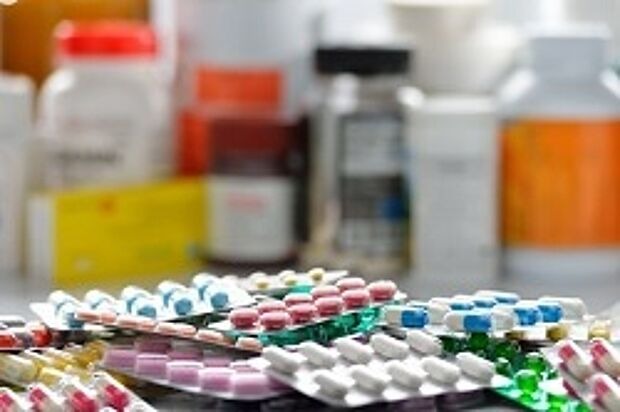 Im Vordergrund gehäuft Tabletten in Sichtverpackung, im Hintergrund Medikamente in Fläschchen
